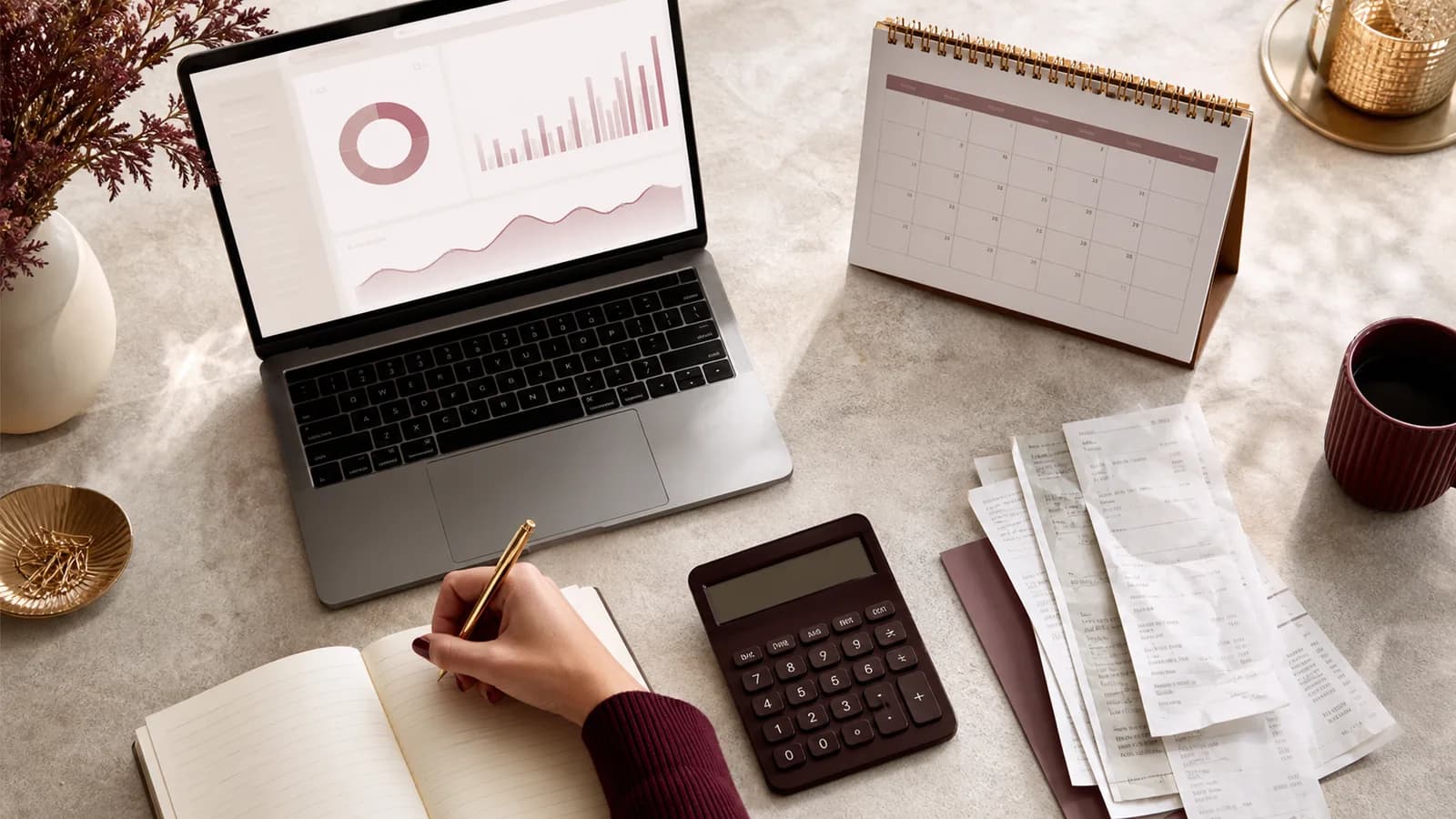 Studioinhaberin plant laufende Websitekosten mit Kalender, Laptop und geordneten Belegen.